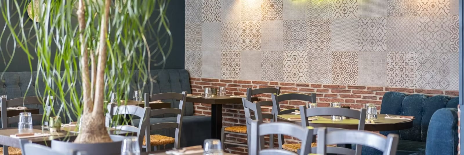 Salle du restaurant Le Gondi : banquettes en velours bleu pétrole, mur de carreaux de ciment et brique apparente, tables dressées.