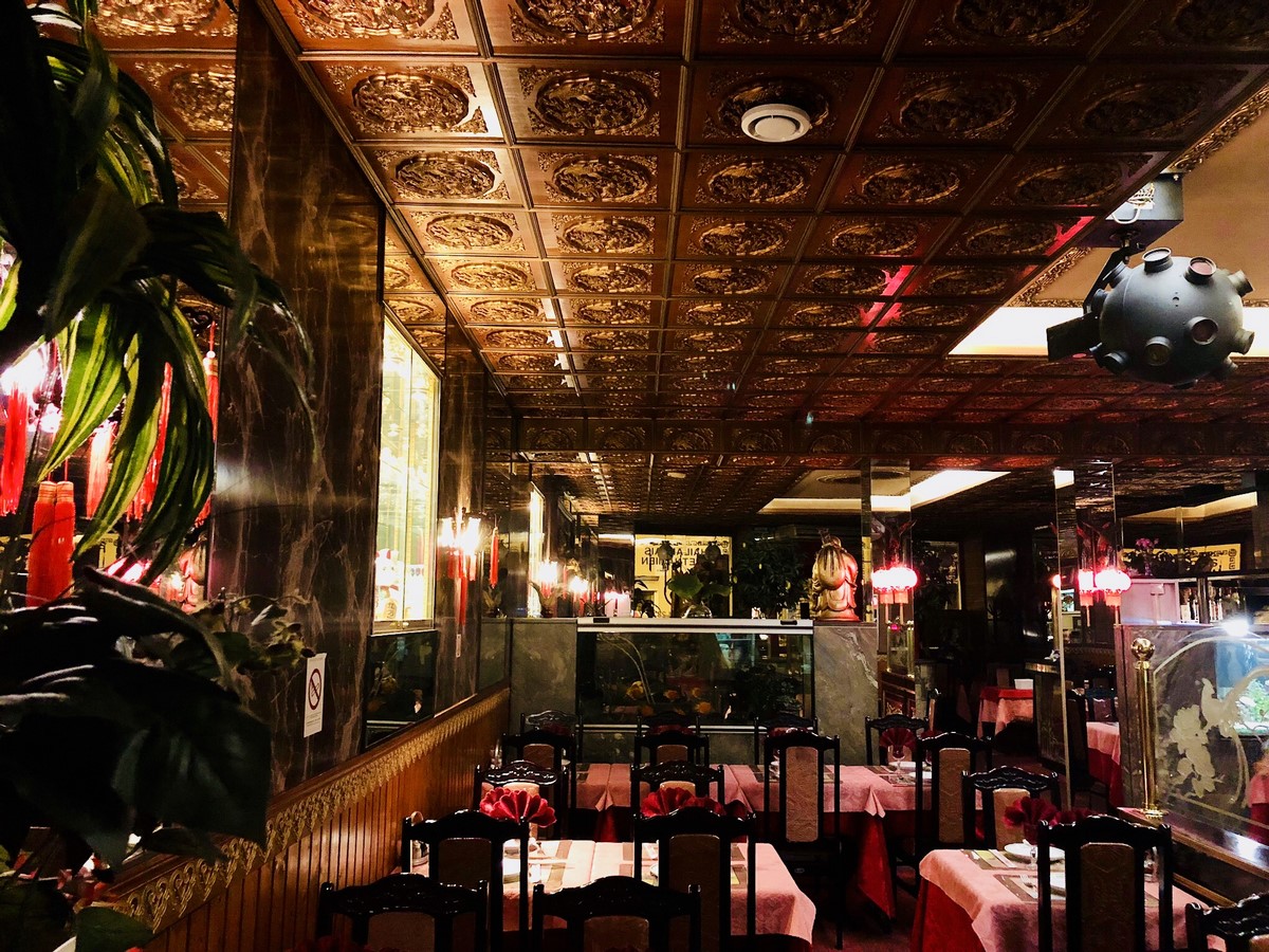 Salle du restaurant : plafond sculpté doré, lanternes rouges, tables nappées et boiseries.