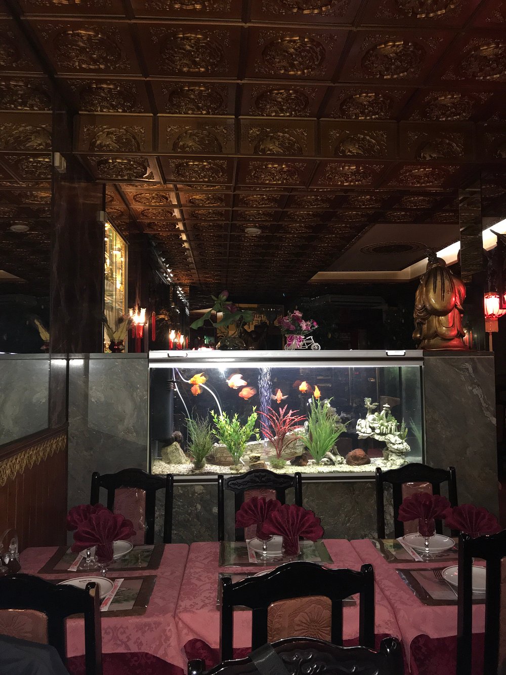 Coin salle avec grand aquarium éclairé, plafond doré sculpté et tables dressées.